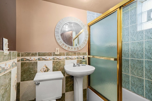 bathroom with toilet, combined bath / shower with glass door, and tile walls