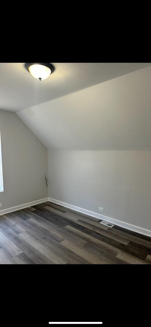 bonus room with dark wood finished floors, baseboards, lofted ceiling, and visible vents