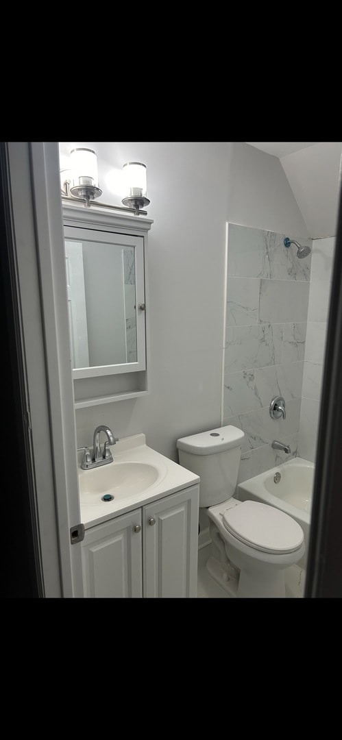 full bathroom with toilet, vanity, tiled shower / bath, and vaulted ceiling