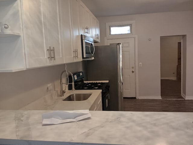 kitchen with baseboards, a sink, white cabinets, appliances with stainless steel finishes, and wood finished floors