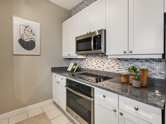 kitchen featuring light tile patterned flooring, stainless steel appliances, dark stone counters, white cabinetry, and backsplash