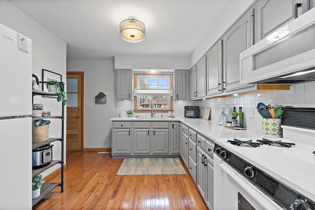 kitchen featuring gray cabinetry, sink, white appliances, and light wood-type flooring