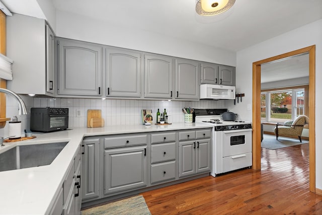 kitchen with hardwood / wood-style floors, white appliances, gray cabinetry, and sink