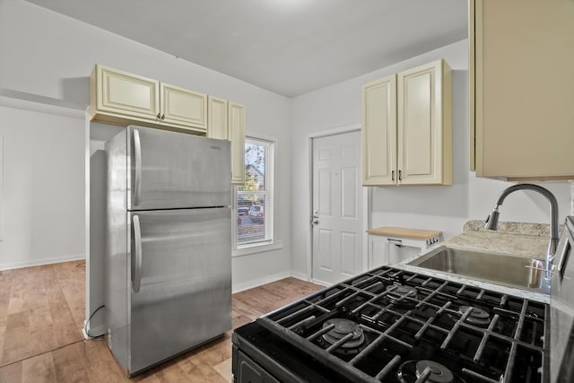 kitchen with light wood-type flooring, cream cabinets, sink, and stainless steel refrigerator