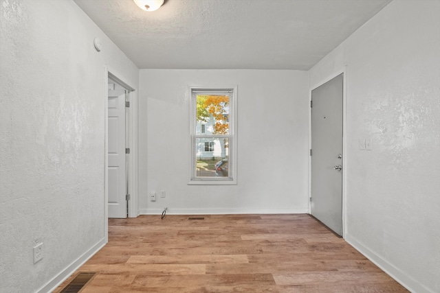 empty room with a textured ceiling and light hardwood / wood-style flooring