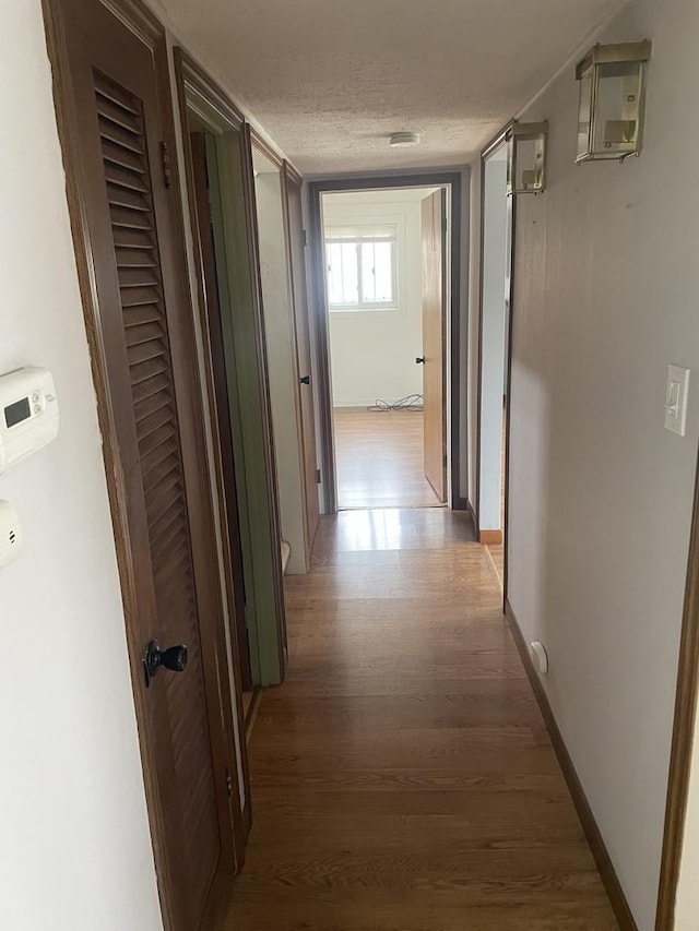 corridor with a textured ceiling and hardwood / wood-style flooring