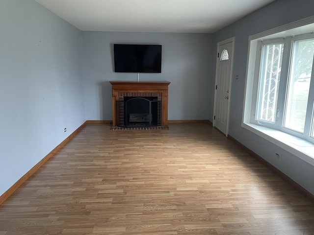 unfurnished living room featuring a healthy amount of sunlight, light wood-type flooring, and a brick fireplace