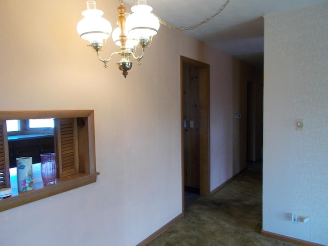 hallway featuring dark colored carpet and a notable chandelier