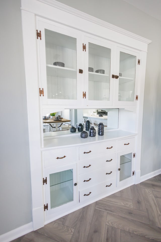 bar with white cabinets and dark parquet flooring