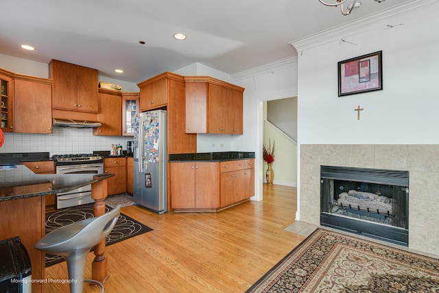 kitchen featuring appliances with stainless steel finishes, ornamental molding, ventilation hood, light hardwood / wood-style flooring, and a tile fireplace