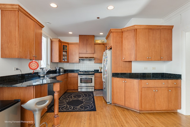 kitchen featuring light hardwood / wood-style floors, dark stone counters, kitchen peninsula, sink, and appliances with stainless steel finishes