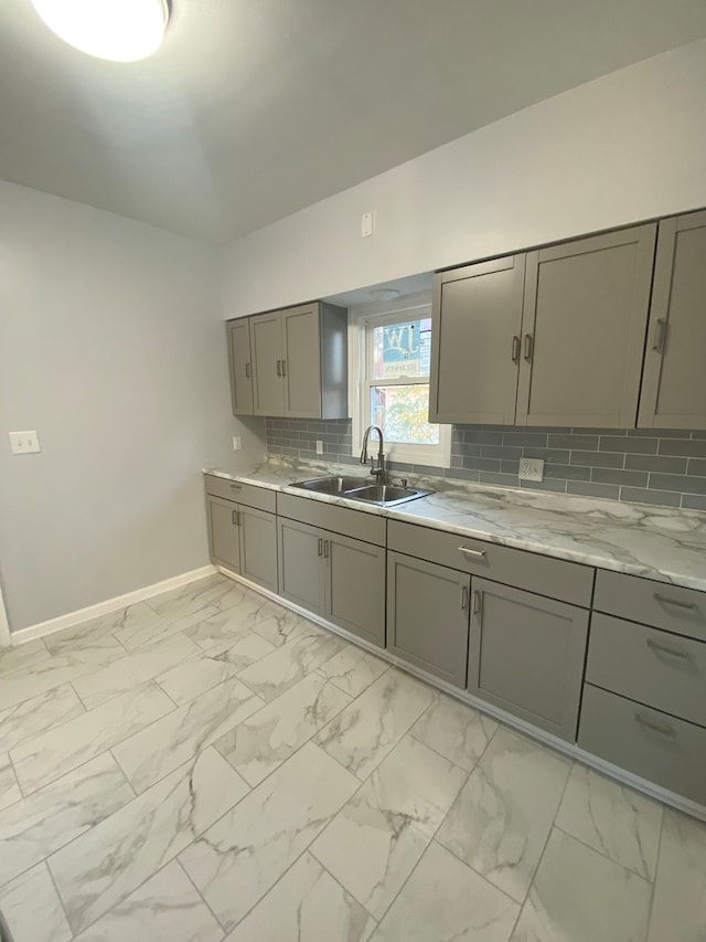 kitchen featuring light stone countertops, sink, backsplash, and gray cabinetry