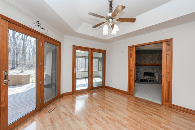 unfurnished room with crown molding, a stone fireplace, light hardwood / wood-style floors, and a raised ceiling