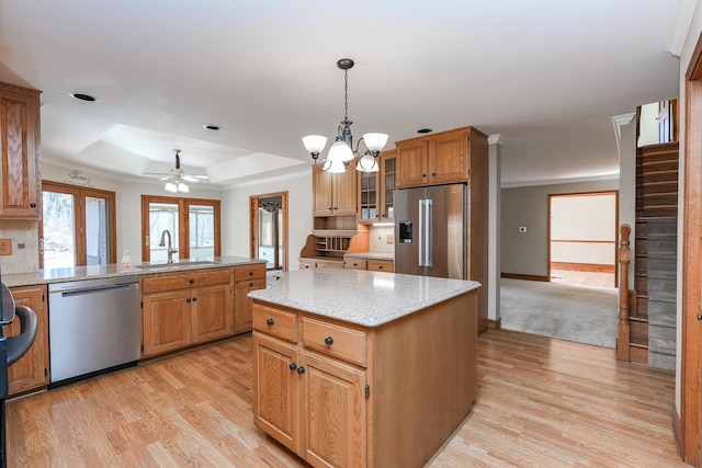 kitchen featuring sink, appliances with stainless steel finishes, a raised ceiling, a kitchen island, and light hardwood / wood-style floors