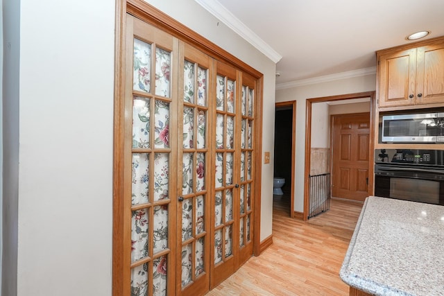 kitchen with stainless steel microwave, oven, ornamental molding, light stone counters, and light hardwood / wood-style flooring