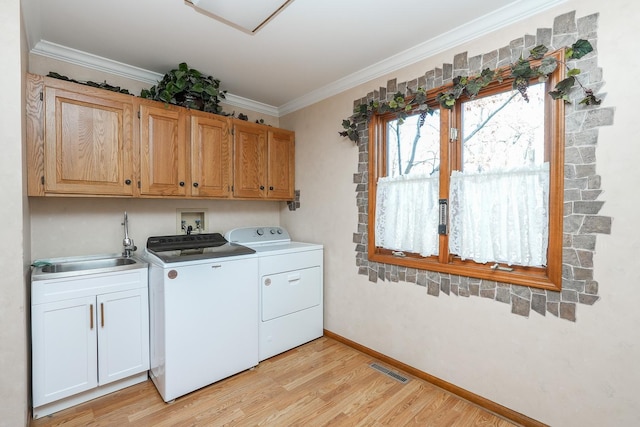 clothes washing area featuring sink, cabinets, washing machine and clothes dryer, crown molding, and light hardwood / wood-style flooring