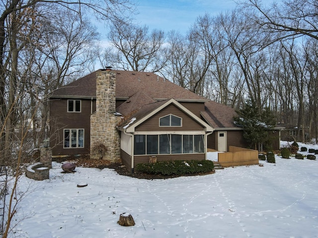 snow covered rear of property with a deck and a sunroom