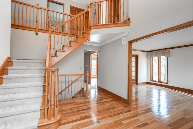 stairway with a towering ceiling, wood-type flooring, and ornamental molding