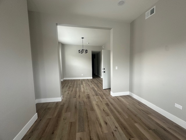 empty room featuring dark wood-type flooring and a chandelier