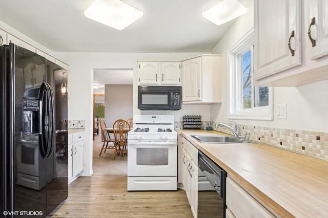 kitchen featuring white cabinetry, sink, tasteful backsplash, black appliances, and light wood-type flooring