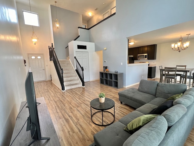 living room with a towering ceiling, an inviting chandelier, and light wood-type flooring