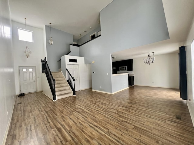 unfurnished living room with hardwood / wood-style floors, a chandelier, and a high ceiling