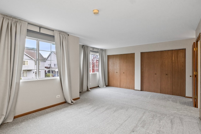 unfurnished bedroom featuring light colored carpet, multiple windows, and two closets