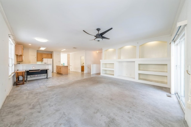 unfurnished living room featuring ornamental molding, light colored carpet, ceiling fan, a healthy amount of sunlight, and built in shelves