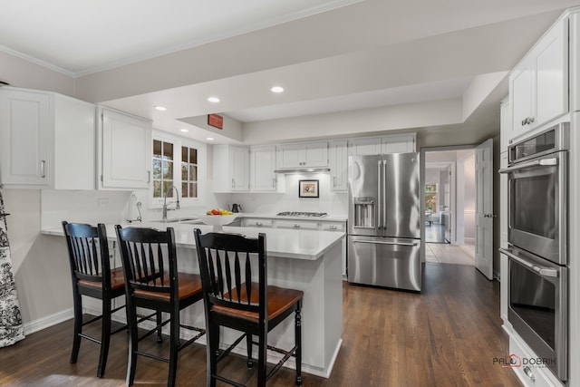 kitchen with a breakfast bar, white cabinets, dark hardwood / wood-style floors, appliances with stainless steel finishes, and kitchen peninsula