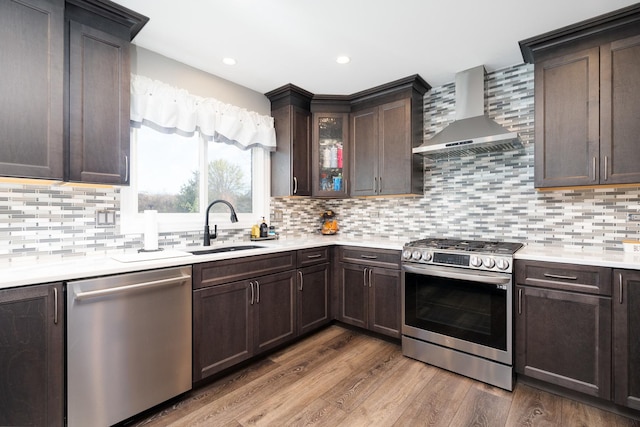 kitchen featuring wall chimney exhaust hood, dark brown cabinetry, sink, appliances with stainless steel finishes, and hardwood / wood-style flooring