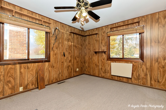 carpeted spare room with wood walls and ceiling fan