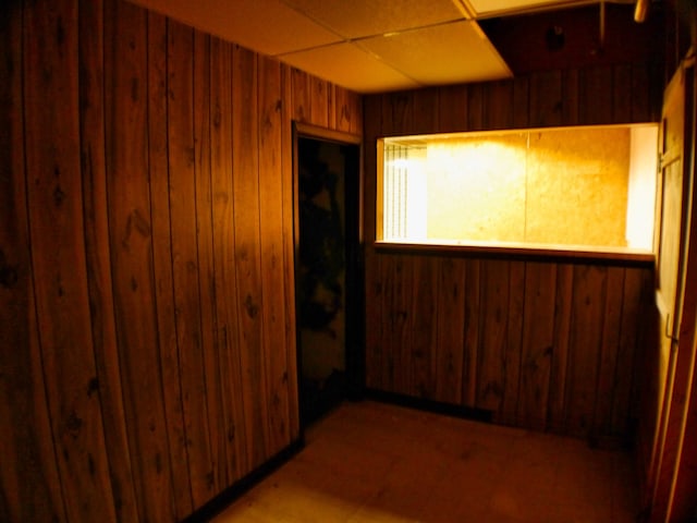 unfurnished room featuring a paneled ceiling and wooden walls