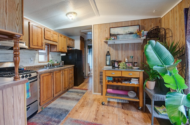 kitchen featuring stainless steel gas stove, black fridge, wood walls, light hardwood / wood-style floors, and vaulted ceiling