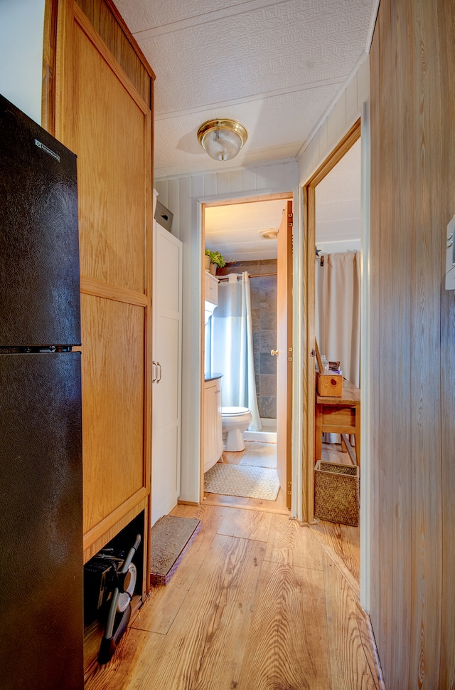 hallway featuring wood walls, light hardwood / wood-style flooring, and a textured ceiling