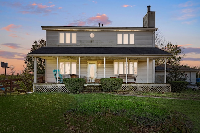 back house at dusk featuring a yard and covered porch