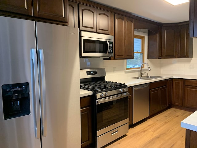 kitchen with stainless steel appliances, sink, backsplash, and light hardwood / wood-style flooring