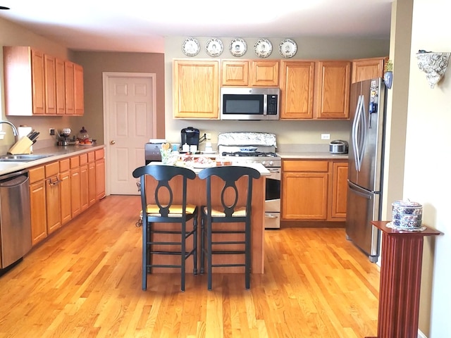 kitchen with a breakfast bar, sink, light hardwood / wood-style flooring, and appliances with stainless steel finishes