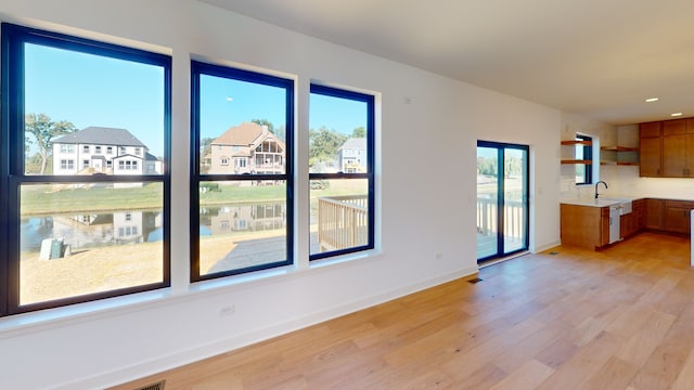 unfurnished living room with light hardwood / wood-style flooring, a water view, and sink