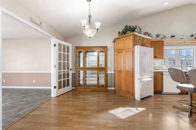 kitchen with white appliances, an inviting chandelier, light hardwood / wood-style flooring, vaulted ceiling, and decorative light fixtures