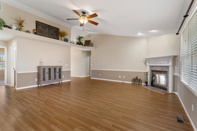 unfurnished living room with a tile fireplace, a wealth of natural light, ceiling fan, and hardwood / wood-style flooring