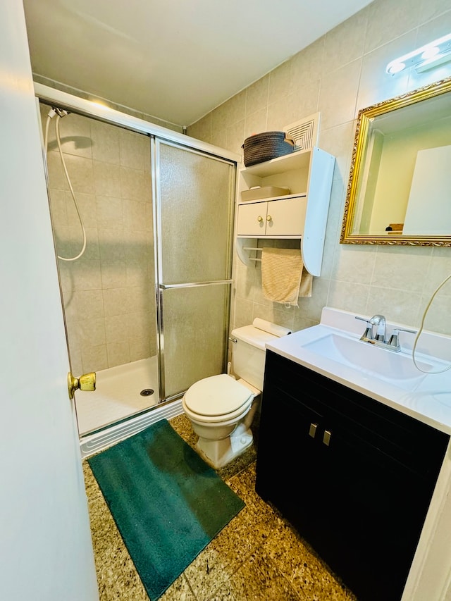 bathroom with tile walls, vanity, toilet, and a shower with shower door