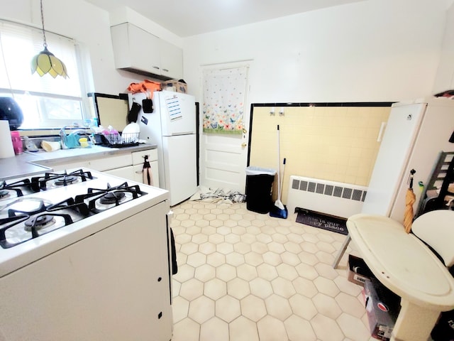 kitchen featuring white cabinets, hanging light fixtures, white appliances, and radiator