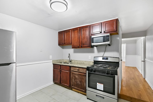 kitchen with light stone countertops, sink, light hardwood / wood-style floors, and appliances with stainless steel finishes