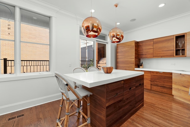 kitchen featuring hardwood / wood-style floors, a breakfast bar, pendant lighting, and crown molding