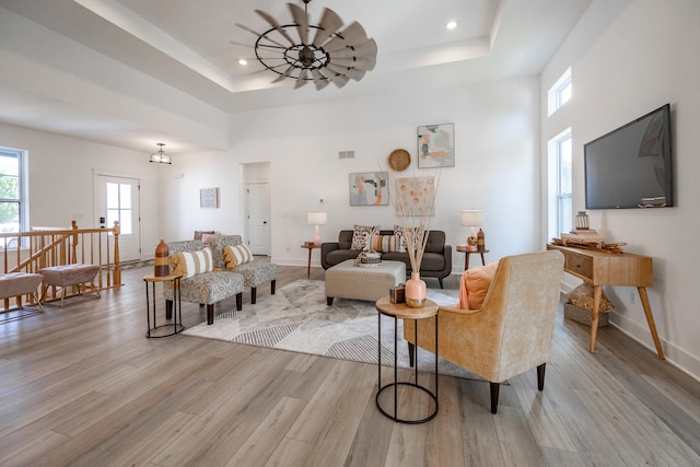 living room with light hardwood / wood-style floors, a towering ceiling, and a tray ceiling