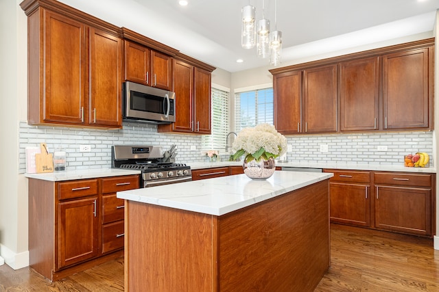 kitchen featuring hanging light fixtures, hardwood / wood-style flooring, decorative backsplash, and appliances with stainless steel finishes