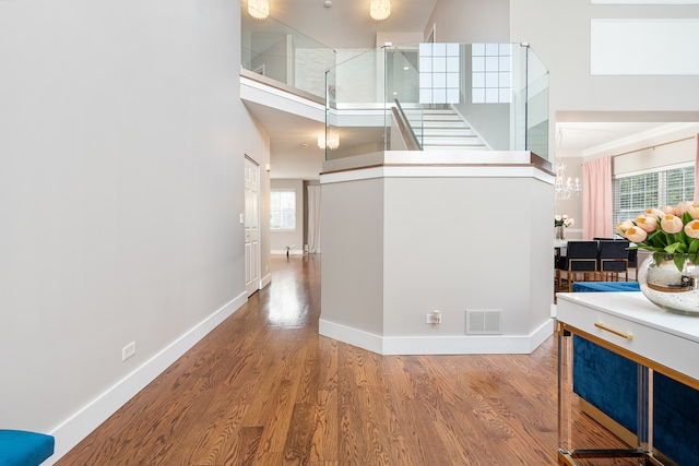 hall featuring ornamental molding, hardwood / wood-style floors, a chandelier, and a high ceiling