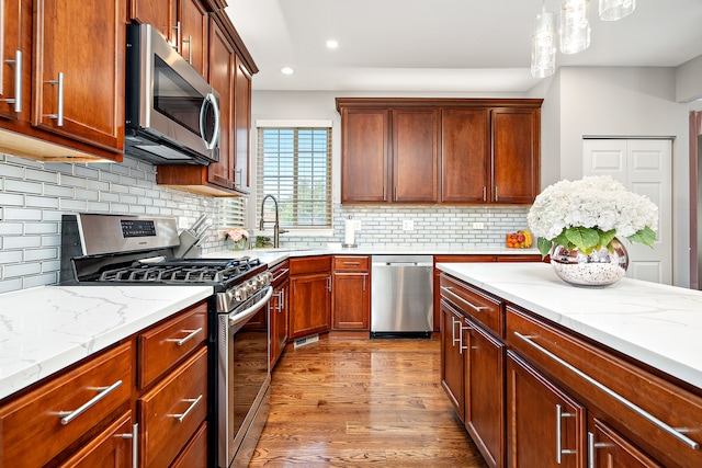 kitchen with light wood-type flooring, stainless steel appliances, decorative light fixtures, and backsplash