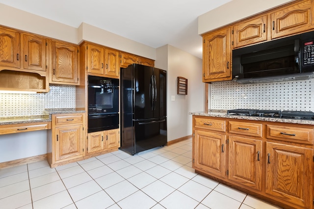 kitchen featuring backsplash, light stone countertops, light tile patterned floors, and black appliances