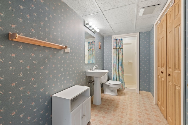 bathroom with a paneled ceiling, curtained shower, sink, tile patterned flooring, and toilet